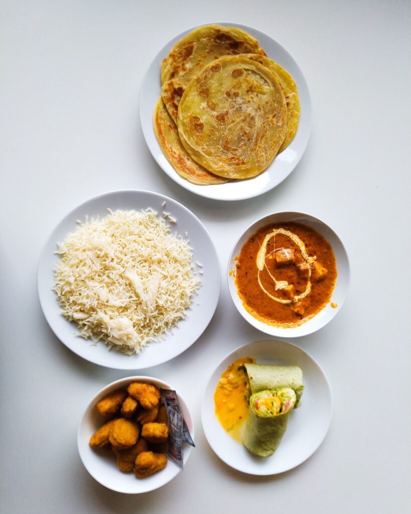 A variety of Indian dishes including paratha, curry, rice, and appetizers served on white plates.