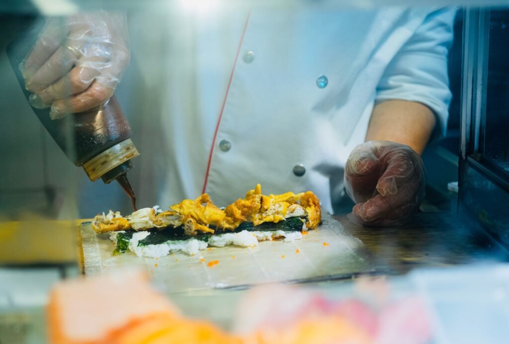 A chef in gloves carefully prepares sushi with sauce, showcasing culinary skills.